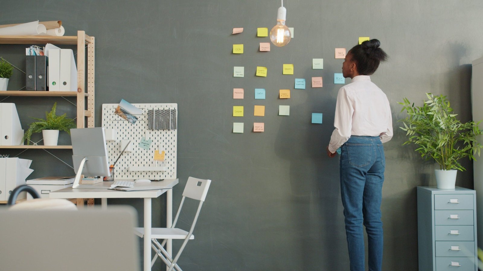Woman arranging sticky notes on office wall for planning or brainstorming.